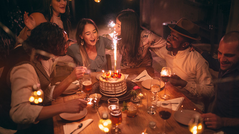 group around table with lit birthday cake