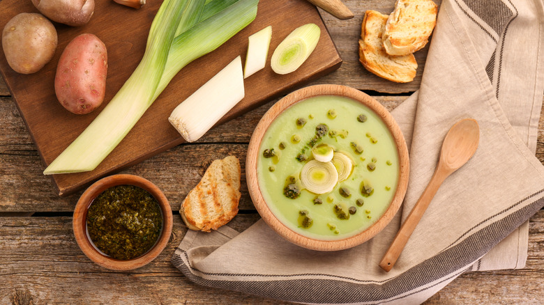 bowl of thick potato leek soup surrounded by potatoes and leeks