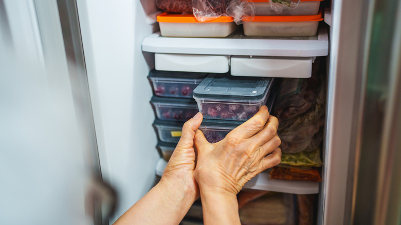Plastic food containers being carefully removed from a freezer