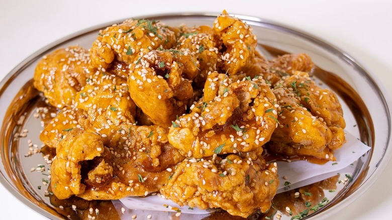 Crispy honey buffalo fried chicken sprinkled with sesame seeds on a stainless steel plate from Han's Chimaek korean style fried chicken restaurant.
