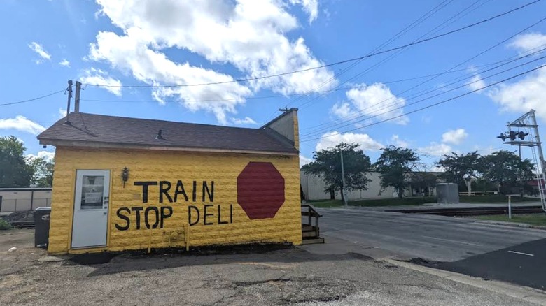 The words Train Stop Deli are painted on the side of this tiny yellow building in Madison County, Indiana at a train crossing.
