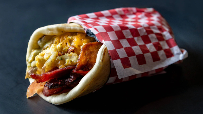 A breakfast gyro from The Gyros Wagon in Dillon, Montana is pictured in classic red and white checkered diner paper, stuffed with scrambled eggs, veggies and bacon.