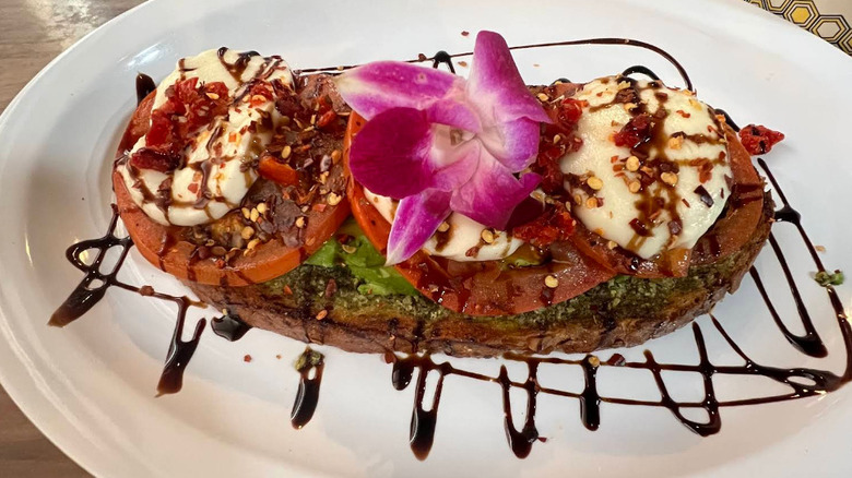 A large piece of avocado toast adorned with tomatoes, chili flakes, cheese, balsamic glaze and a flower, demonstrating the blend of Hawaiian and Southern cuisines available at Junction Remix 580 in Lawton, Oklahoma.