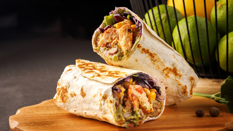 Chicken burrito cut in half displayed on wooden board