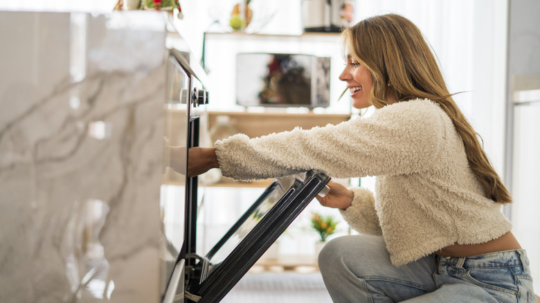woman smiling reaching into an open oven