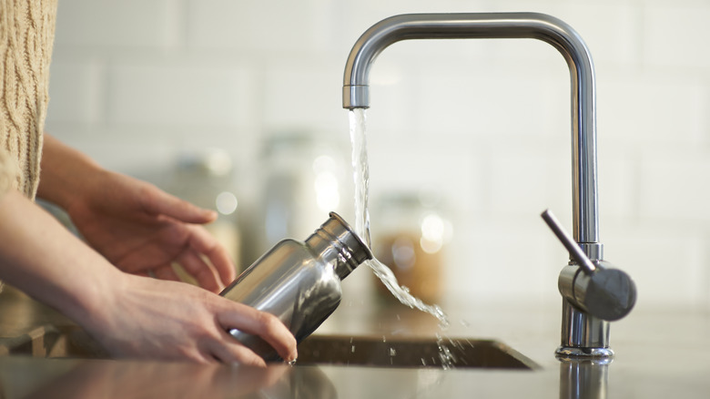 Person cleaning water bottle in kitchen sink