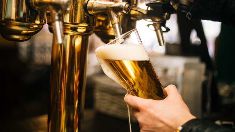 Pouring a glass of light-colored beer from a gold-colored beer tap