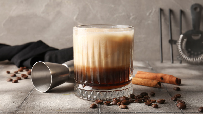 A white Russian cocktail with cinnamon sticks and coffee beans