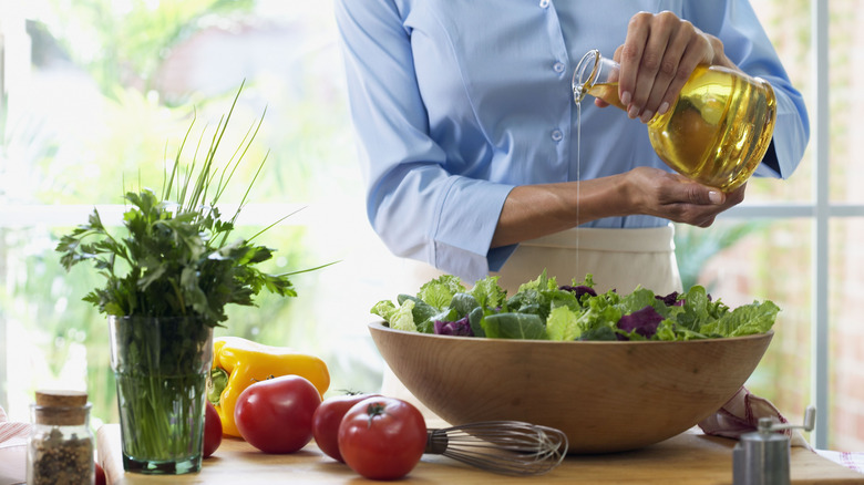 Person pouring oil onto a bowl of salad