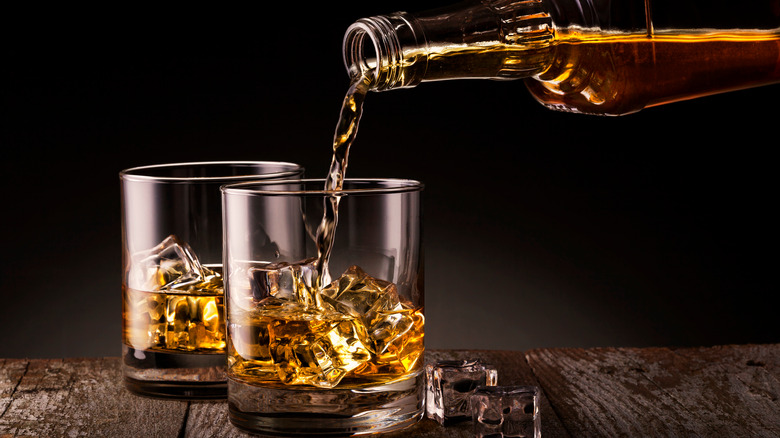 pouring whiskey into a glass with ice