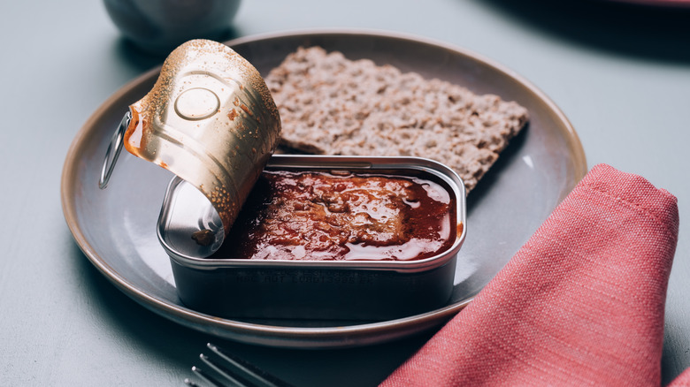 Opened can of fish in tomato sauce on a plate with a cracker
