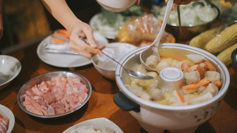 Hands spooning hot pot broth