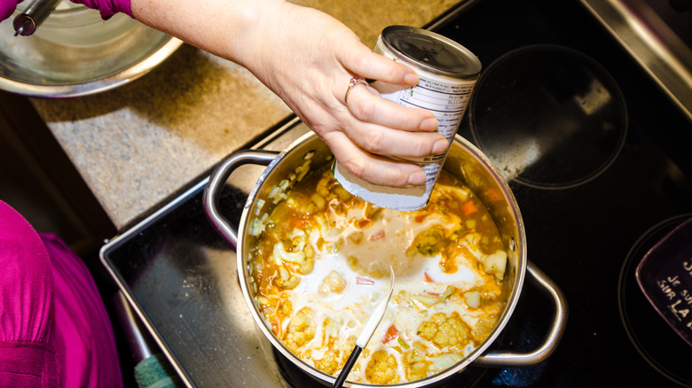 Woman adding coconut milk to soup