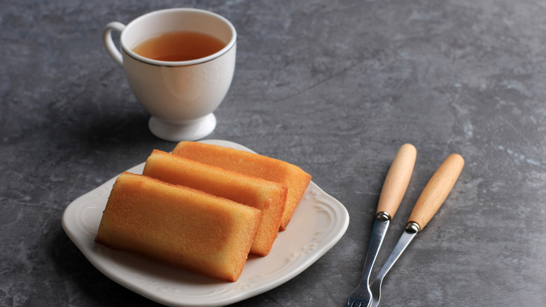 Three financier cakes on a plate by a cup of tea