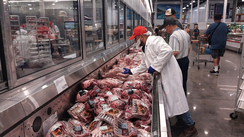 A butcher arranges meats for sale in a Costco store