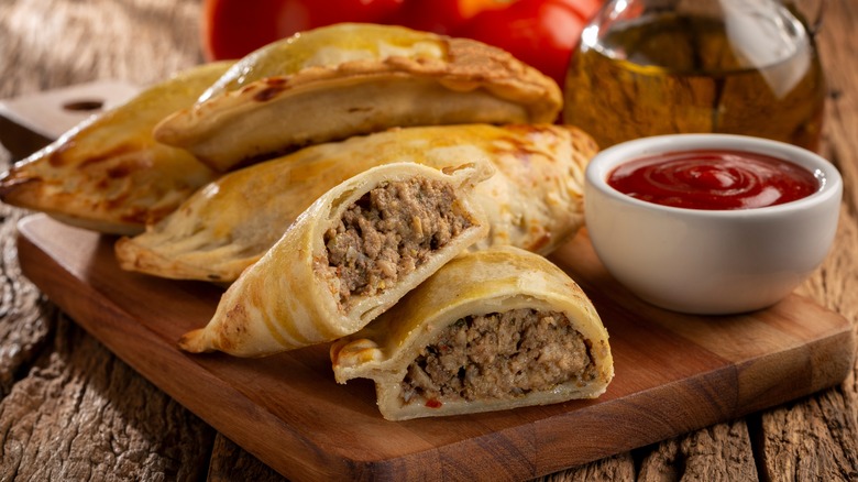 empanadas on a wood cutting board with ketchup on the side