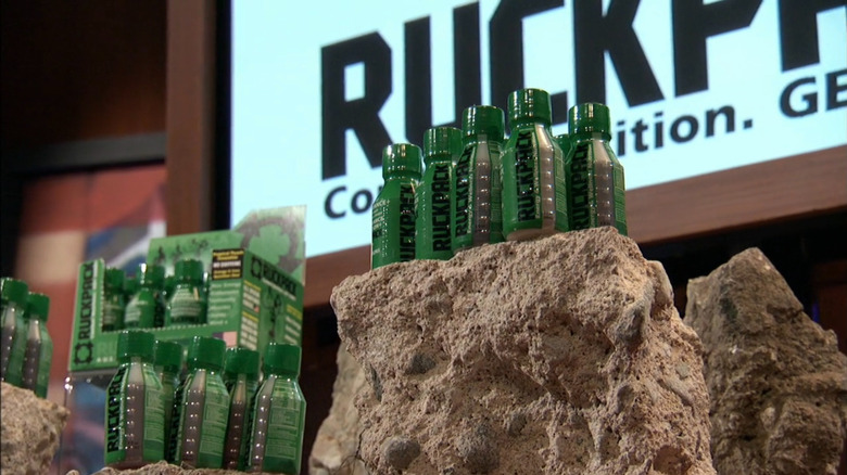 Green shot bottles of RuckPack on a rock on the Shark Tank set