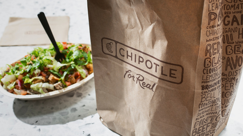 A chicken burrito bowl from Chipotle with a Chipotle bag in the foreground