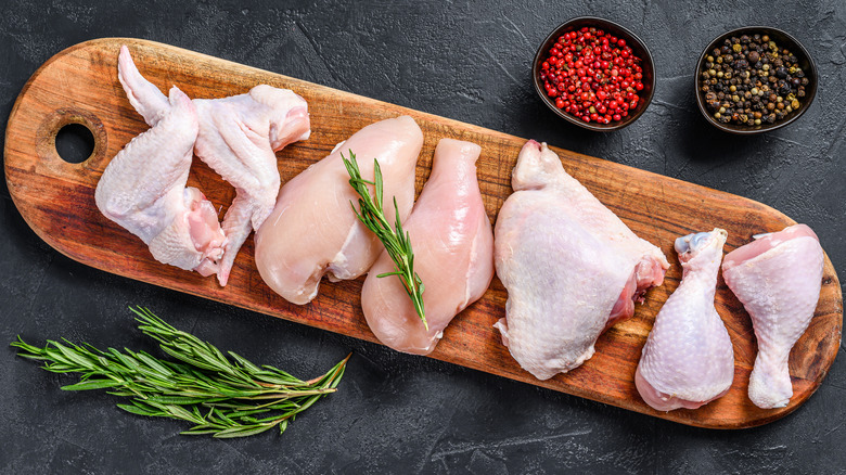 Chicken breasts, wings, and thighs on a wooden cutting board resting on a black slate background