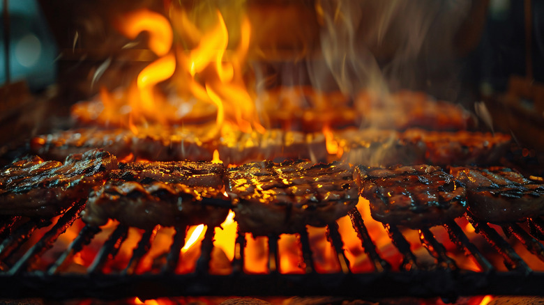 Steaks on a grill with flame.