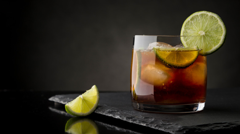 Cuba Libre cocktail with lime wedges and ice