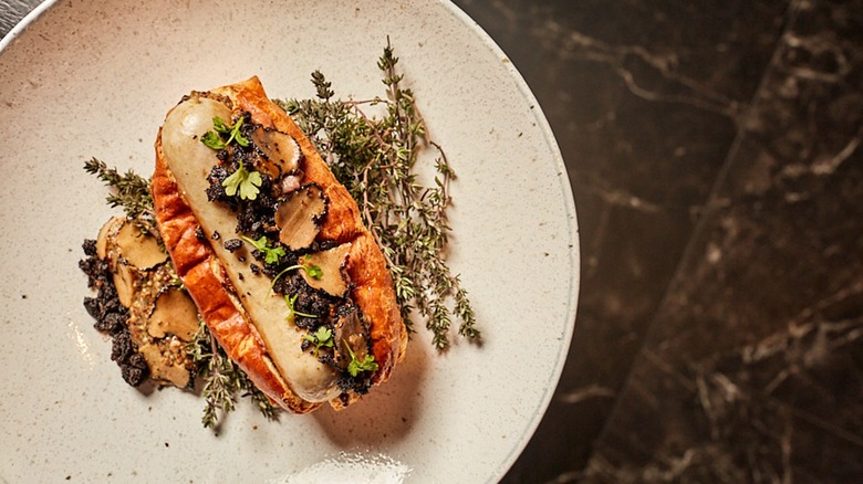 hot dog plated with thyme, truffles, and foie gras