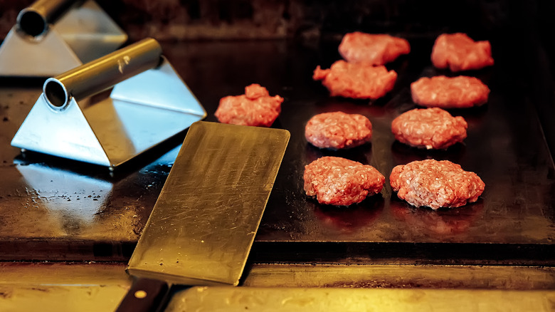small hamburger patties on a griddle with spatula