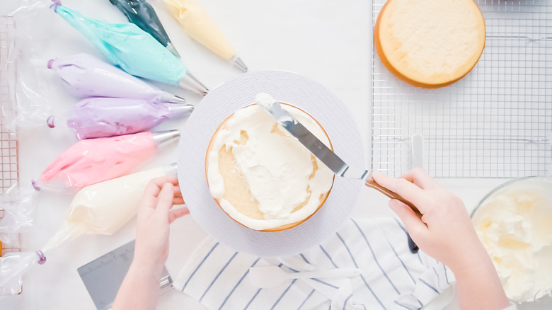Baker spreading icing on cake with multi-colored piping bags