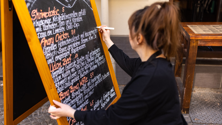 Female writing special menu on the chalkboard outside cafe.