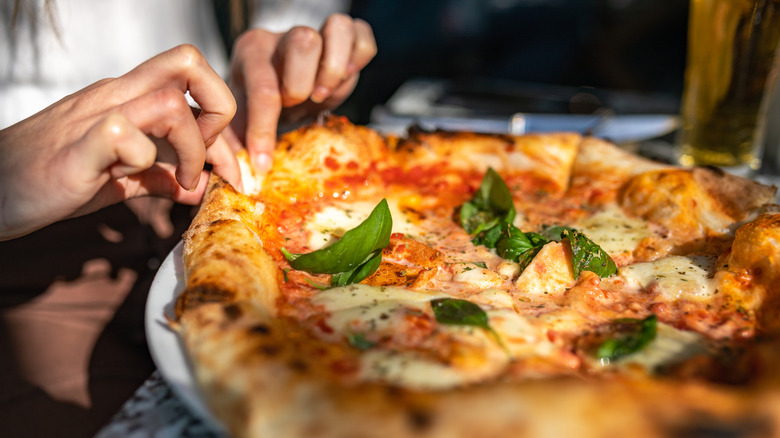 Person taking slice of pizza from whole pie