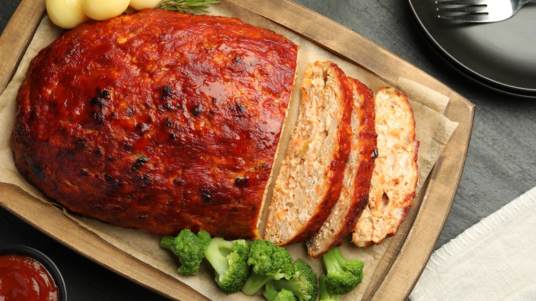 Glazed meatloaf on a wooden cutting board with broccoli and small potatoes