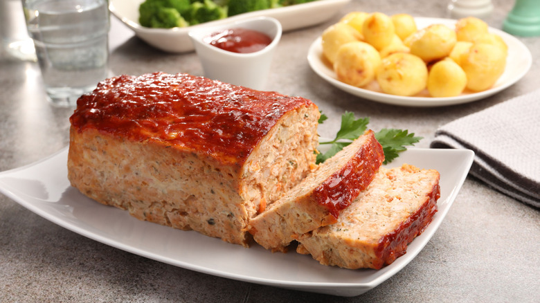 Turkey meatloaf on a white plate with a sprig of parsley with sides in the background