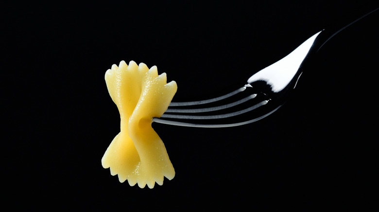 Al dente bowtie pasta on the end of a fork against a black background