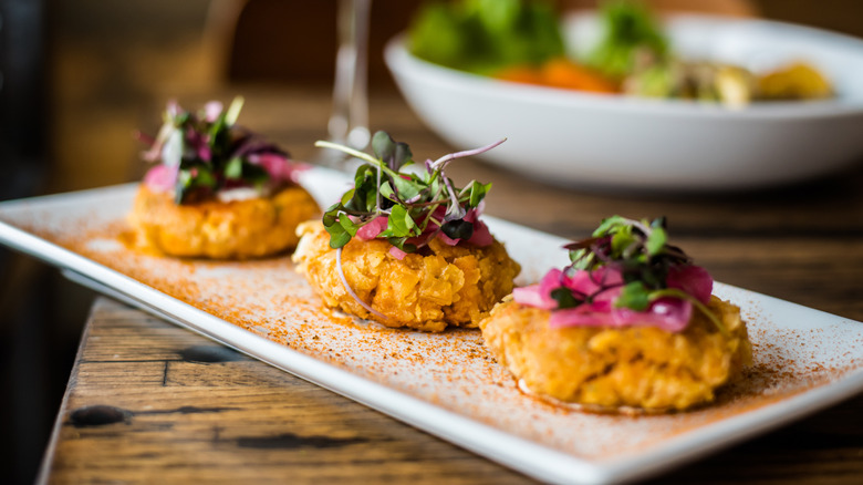 Three small crab cakes on a rectangular plate, topped with fresh greens