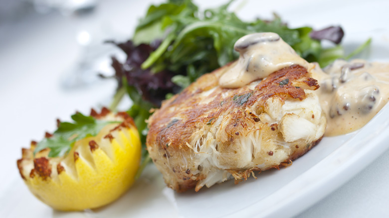 A seared crab cake with a toasted lemon on a fancy white plate
