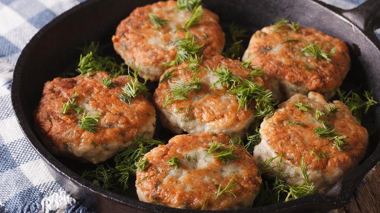 Six crab cakes topped with fresh dill in a cast iron frying pan