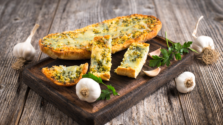 Cheesy garlic bread on a board with garlic bulbs around