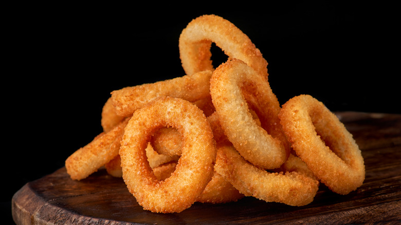 Pile of fried onion rings on a wood board