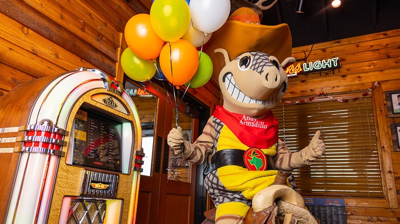 Texas Roadhouse mascot Andy Armadillo posing on a saddle next to the restaurant jukebox with balloons in hand