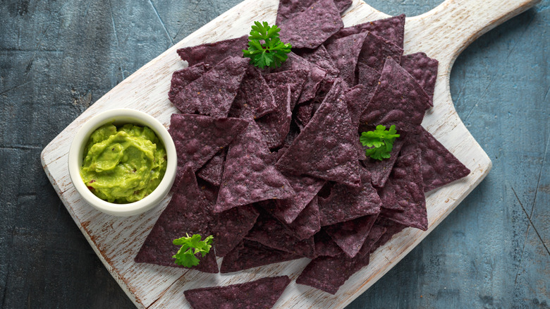 Blue corn tortilla chips on wooden board with guacamole