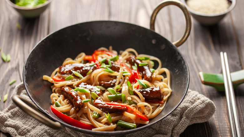 Stir-fried udon noodles in a small wok on a table