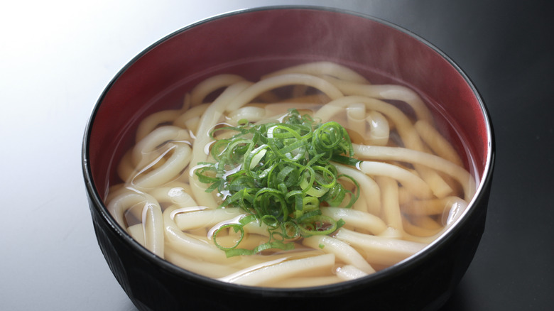 A bowl of hot udon noodle soup topped with chopped spring onions