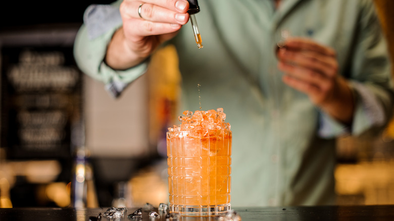 bartender adding dash of bitters to cocktail