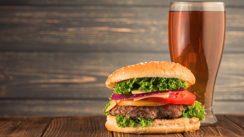 A hamburger topped with vegetables, next to a tall glass of beer