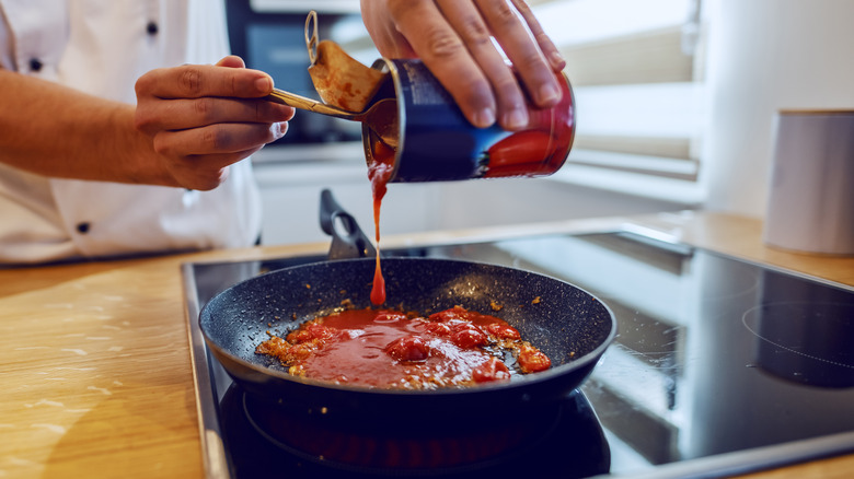 Pouring canned tomatoes into pan