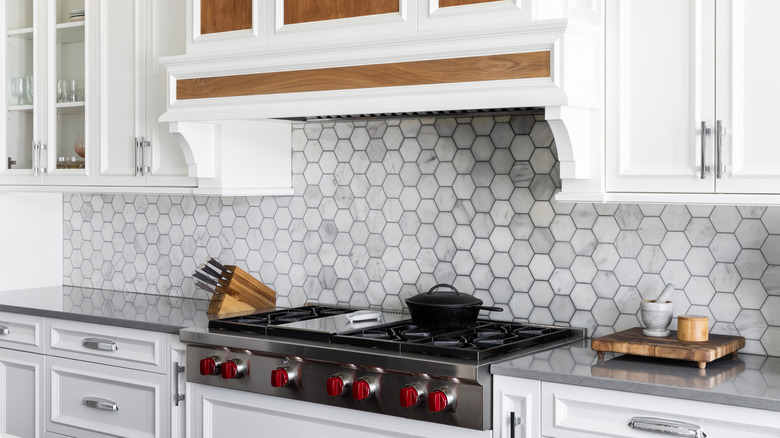 Kitchen with gray and white marble tile backsplash with black grout, dark countertop, and white cabinets
