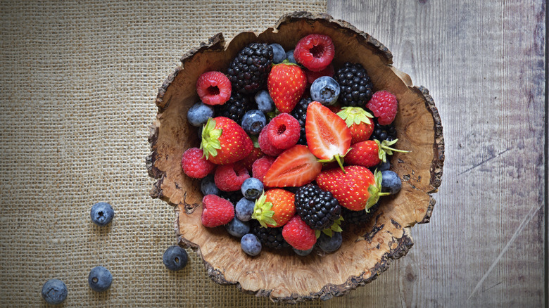 Overview of a natural wood bowl filled with berries on a wood table with a burlap placemat