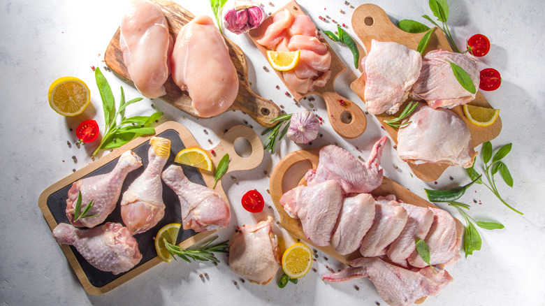 Raw chicken arranged by cut of meat on cutting boards, surrounded by lemons, tomatoes, garlic, and greens