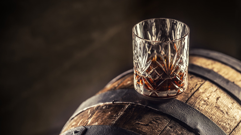 Glass of bourbon on a old wooden barrel.