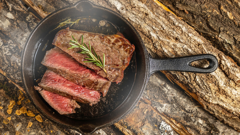 sliced stake in a skillet on wooden planks